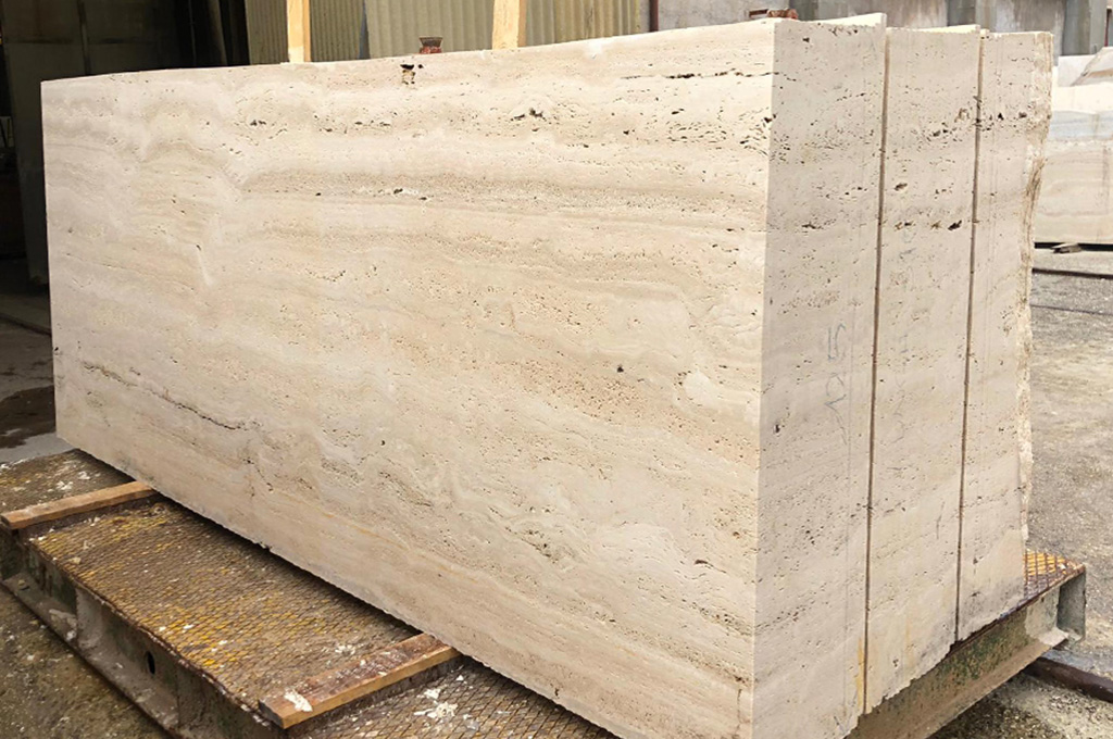 A solid travertine block photographed from the side, its full thickness and vein-cut stratification visible in raking natural light.