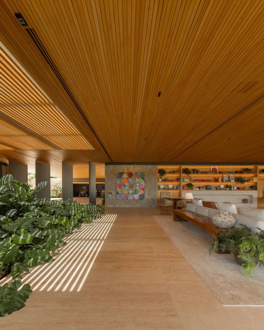 Travertine flooring running from the interior out to the terrace of a house set into a forest reserve, the stone reading as continuous ground beneath full-height glass.