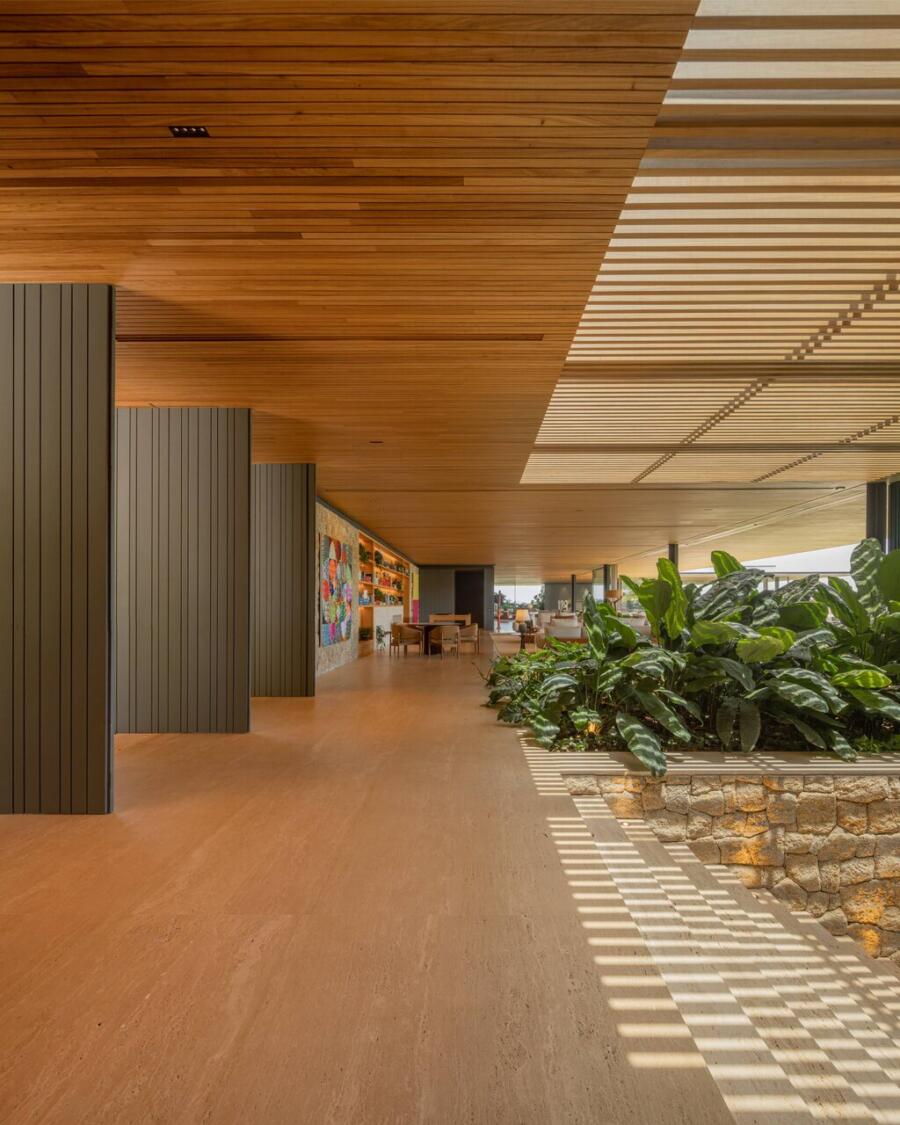 A travertine-floored interior opening to the surrounding forest through large glass panels, the stone holding the room as its quietest, heaviest element.